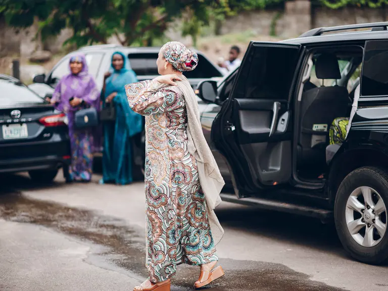 Three women approach a waiting car with its rear door open.